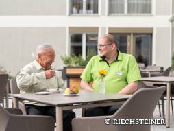 Bewohnender sitzt mit Mitarbeiter und trinkt ein Kaffee