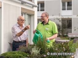 Mitarbeitender mit Bewohner auf der Terrasse am Pflanzen giessen