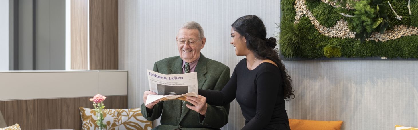 Mitarbeiterin lacht Mann an und schauen gemeinsam die Zeitung an
