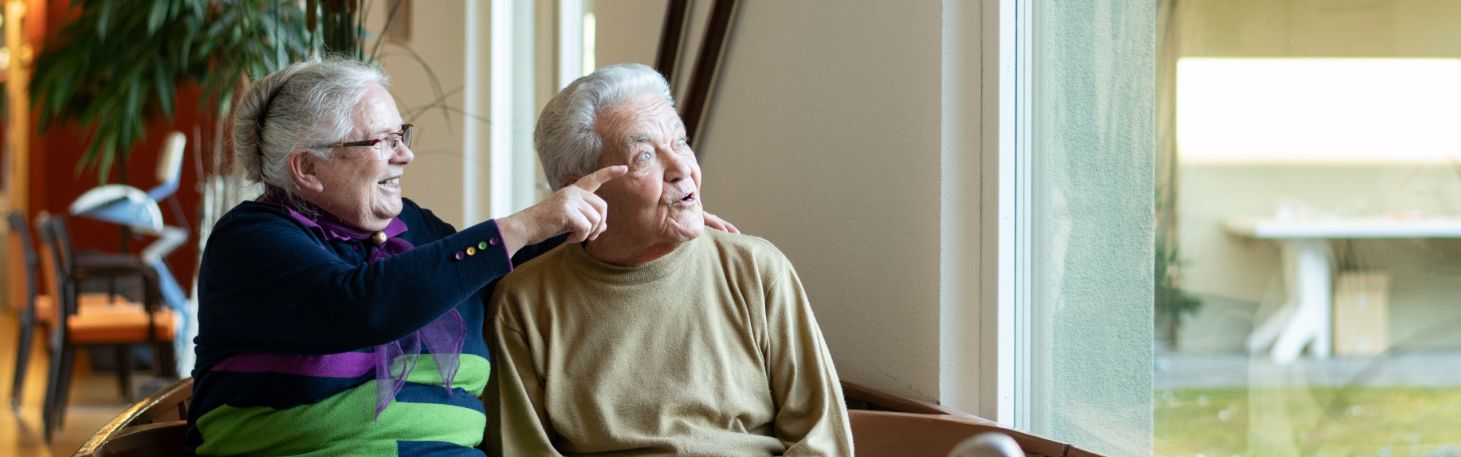 Frau zeigt Person etwas aus dem Fenster