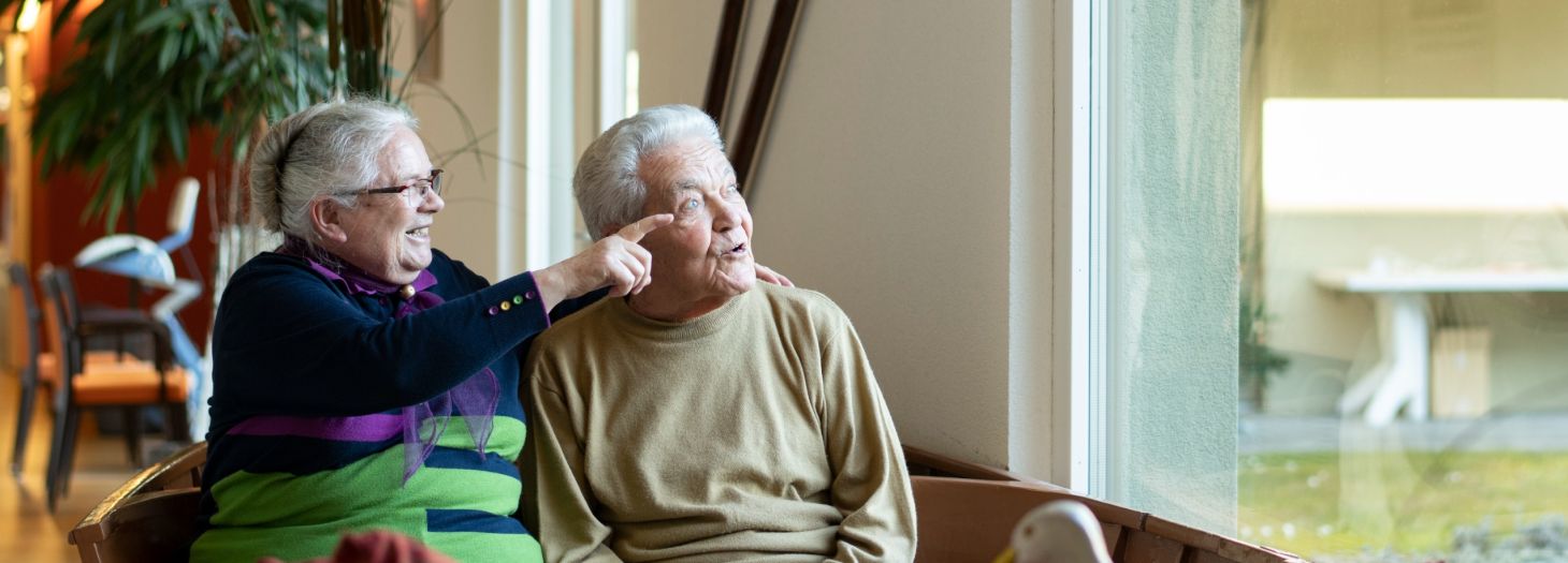 Frau zeigt Person etwas aus dem Fenster