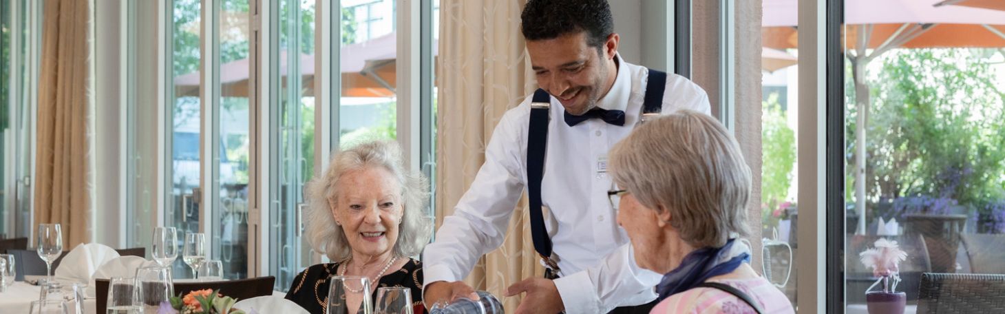 Zwei Herren am Tisch werden vom Servicepersonal zum Mittagessen bedient